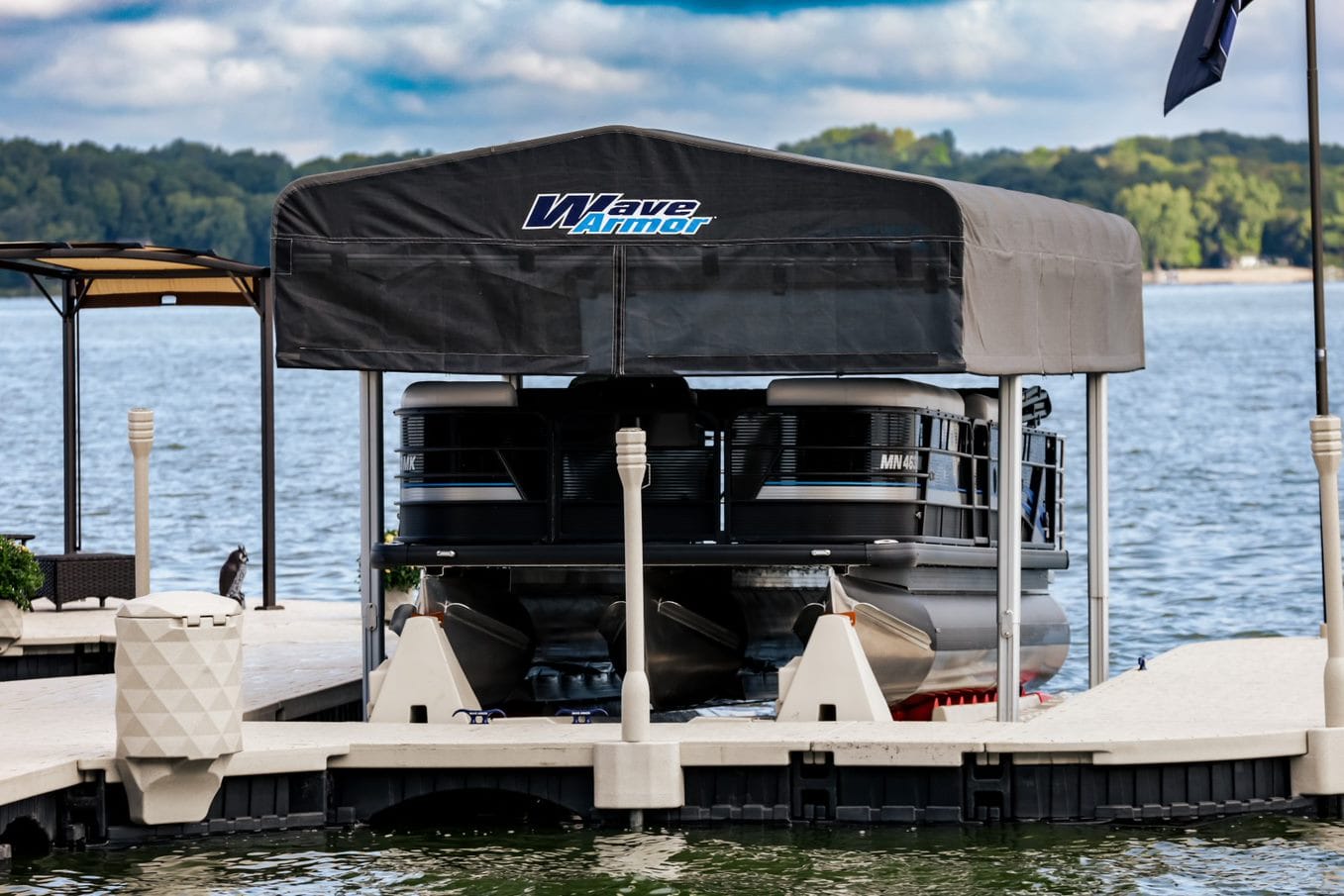 Black pontoon boat parked on a Wave Armor boat lift with canopy cover at a floating dock on a lake.